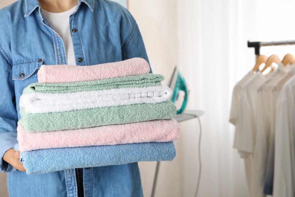 A Woman Is Holding A Pile Of Towels In Her Hands — Buderim Laundrette In Mooloolaba, QLD