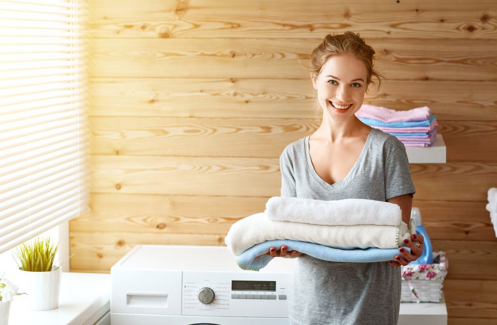 A Woman Is Holding A Pile Of Towels In A Laundry Room — Buderim Laundrette In Buderim, QLD