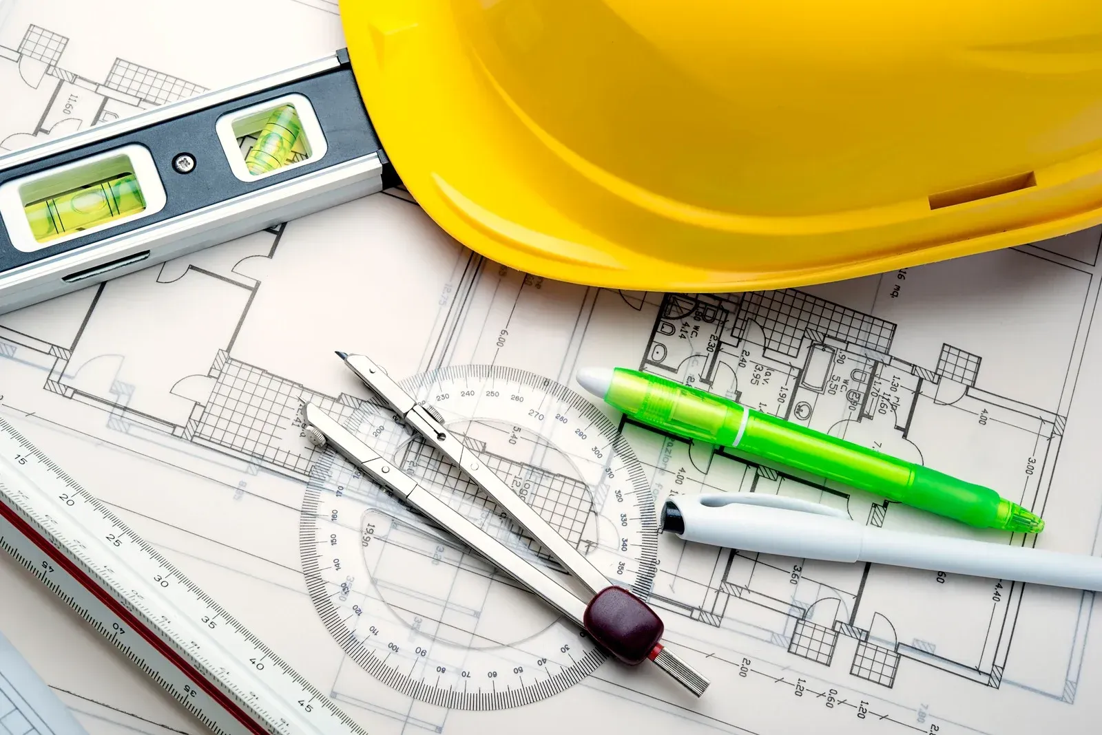 Yellow hard hat, level, blueprints, drafting tools and pens.