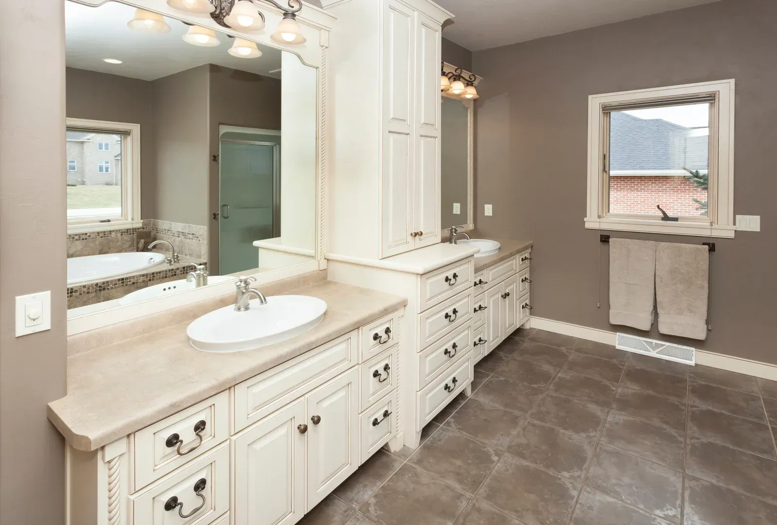 A bathroom with two sinks , two mirrors , and a window.