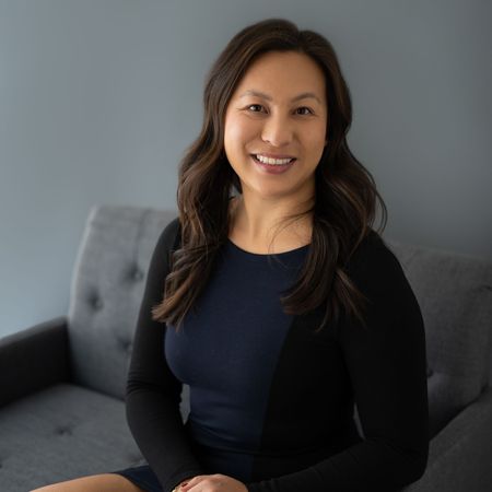 A woman is sitting on a couch wearing a blue dress and a black cardigan.