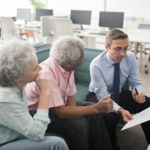 Three coworkers discussing documents in a bright office, with computer monitors in the background.