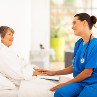 Nurse in blue scrubs talking with a patient in bed in a bright hospital room