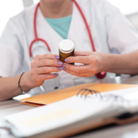 Doctor holding a pill bottle at a desk with a stethoscope and open notebook