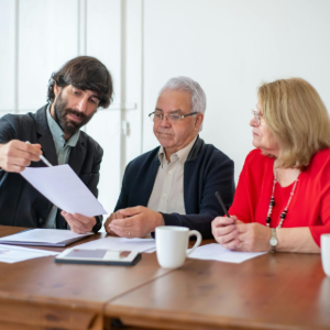 Three coworkers in a meeting reviewing a document at a table with a laptop and coffee mug