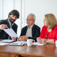 Three coworkers in a meeting reviewing a document at a table with a laptop and coffee mug