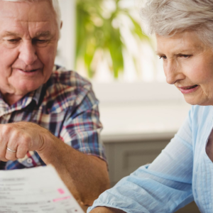 Two older adults reviewing paperwork together at a table, smiling in a bright room