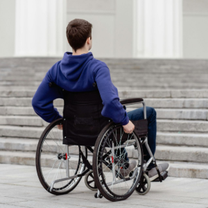 Person in a blue hoodie sits in a wheelchair on stone steps, viewed from behind.