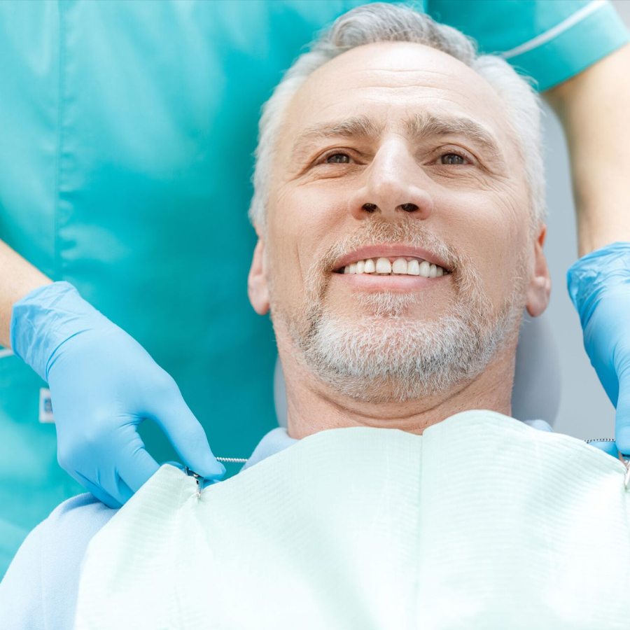 Dental patient smiling while reclining as a dentist adjusts the bib with blue gloves