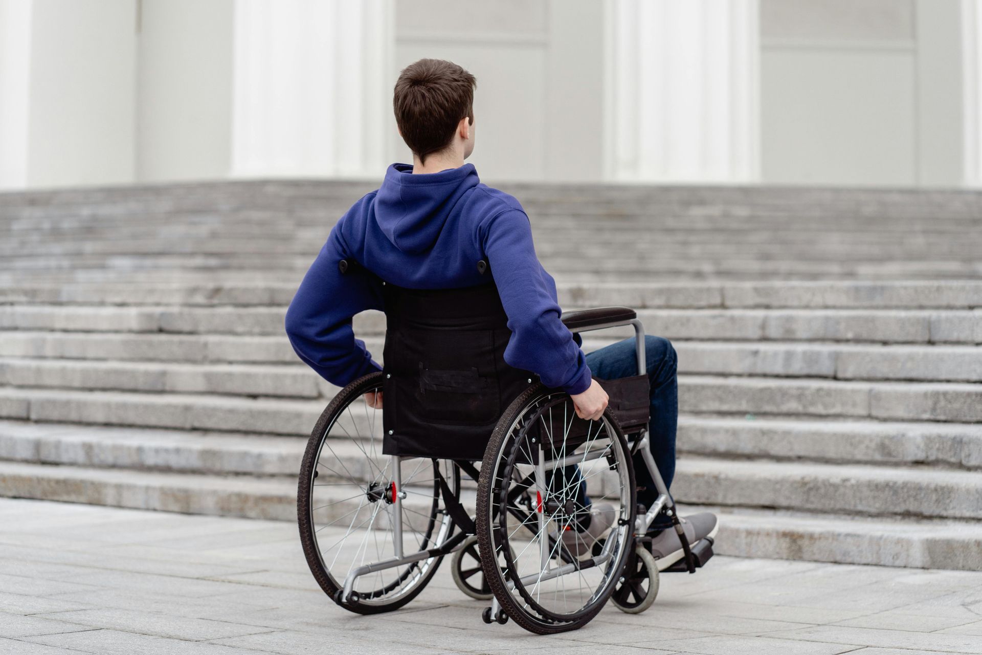 Person in a blue hoodie sitting in a wheelchair facing a set of wide stone steps