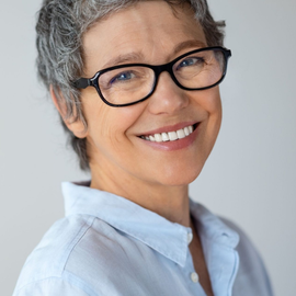 Smiling person in glasses and a light blue shirt against a plain gray background