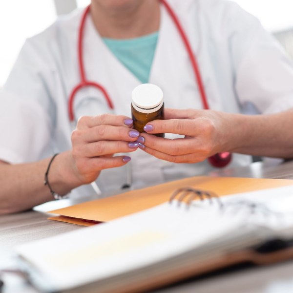 Doctor holding a prescription bottle at a desk with papers and stethoscope