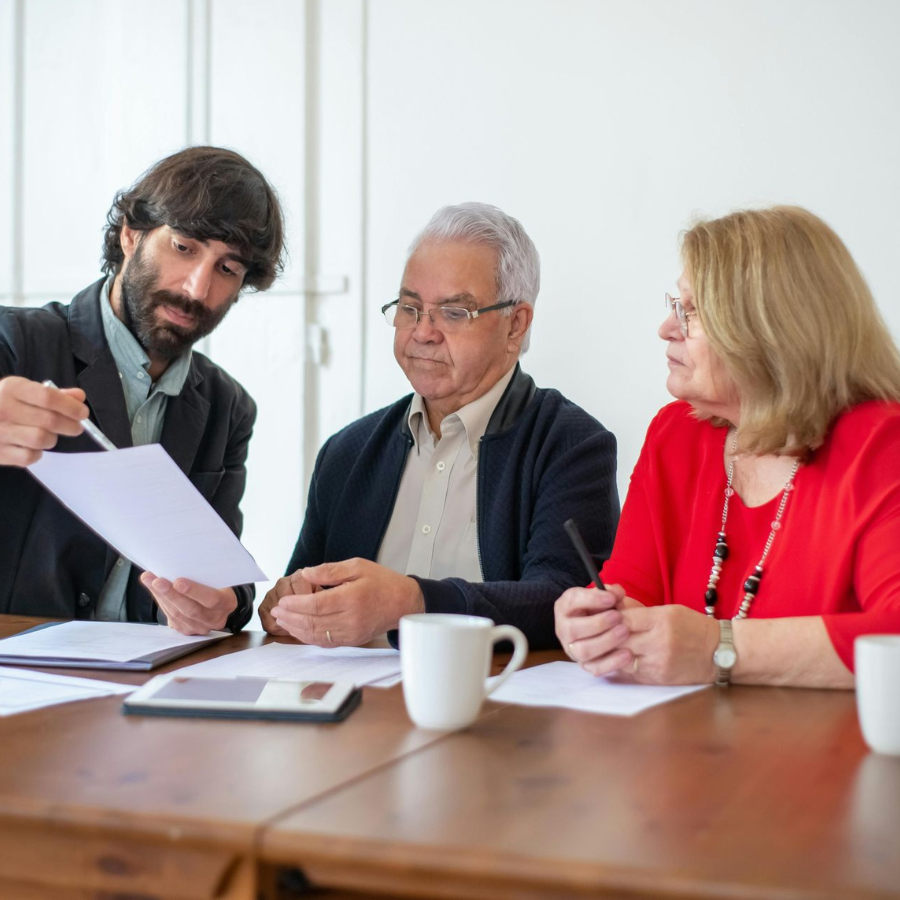 Three people in a meeting reviewing documents at a wooden table with coffee mugs