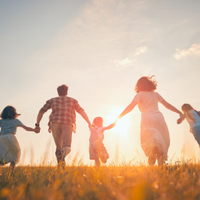Family holding hands and running through a sunlit field at sunset