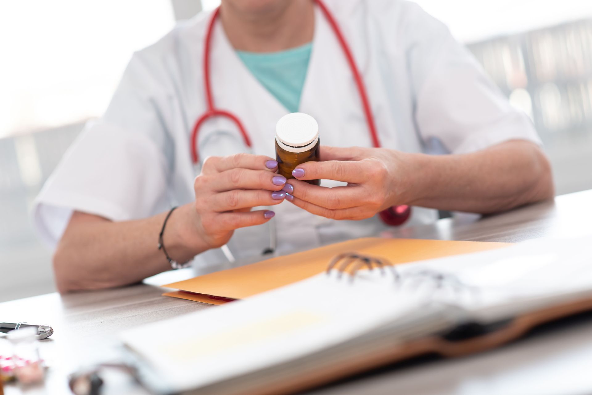 Doctor holding pill bottle at desk with open binder and stethoscope