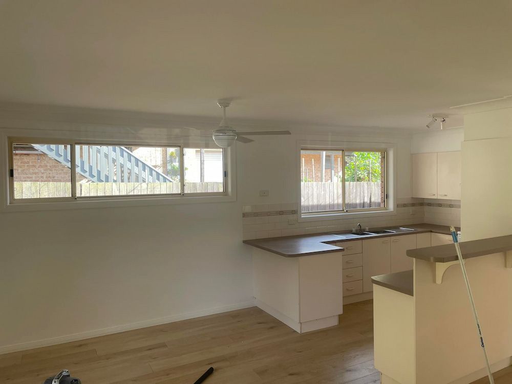 An Empty Kitchen With White Cabinets and a Ceiling Fan — Cornall Painting Services in Port Macquarie, NSW