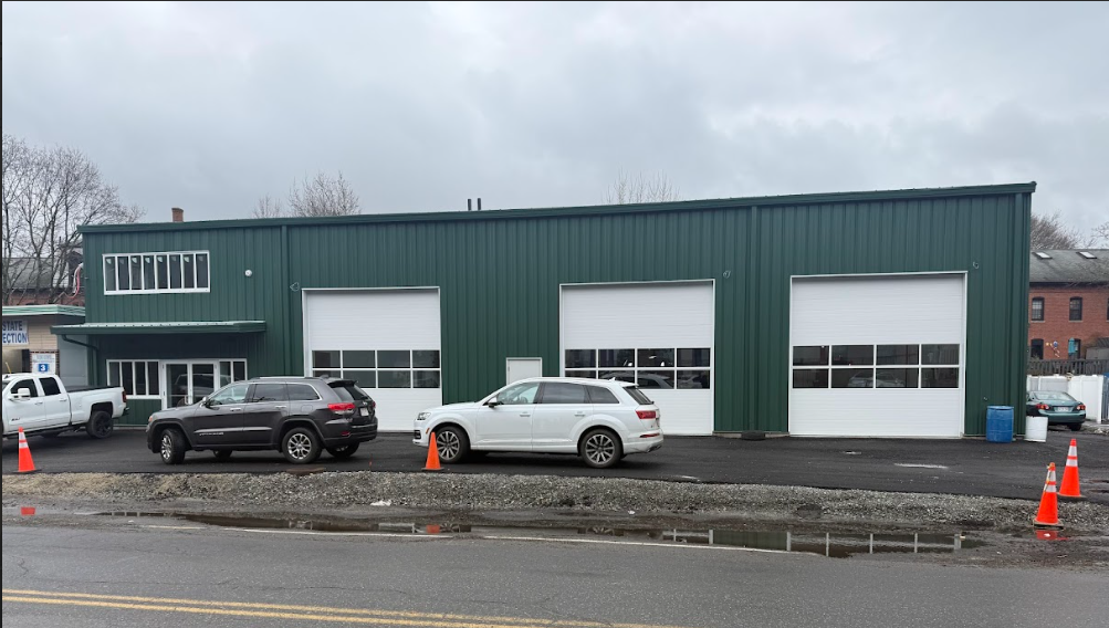 Green building with three garage doors and cars parked in front.