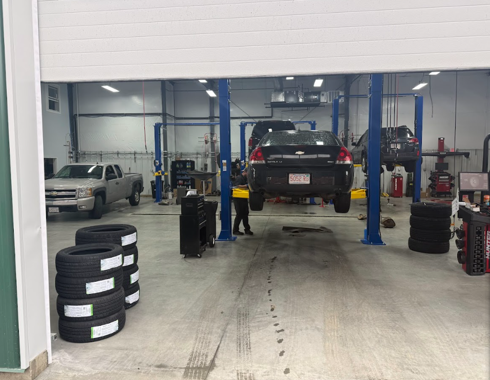 A car repair shop with two cars on lifts and tires stacked on the floor. A person is standing near the car.