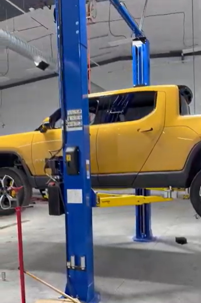 Yellow Rivian truck lifted on a blue hydraulic car lift in a garage.