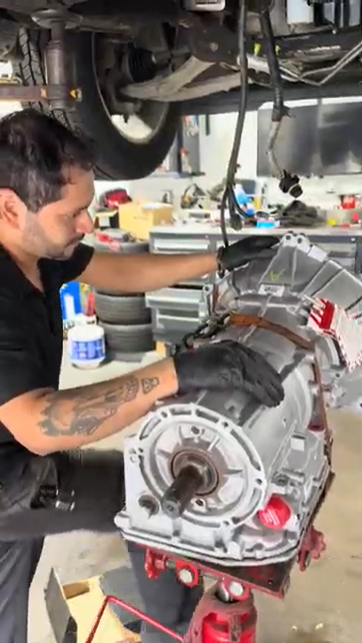 Mechanic working on car transmission in a shop, wearing gloves.