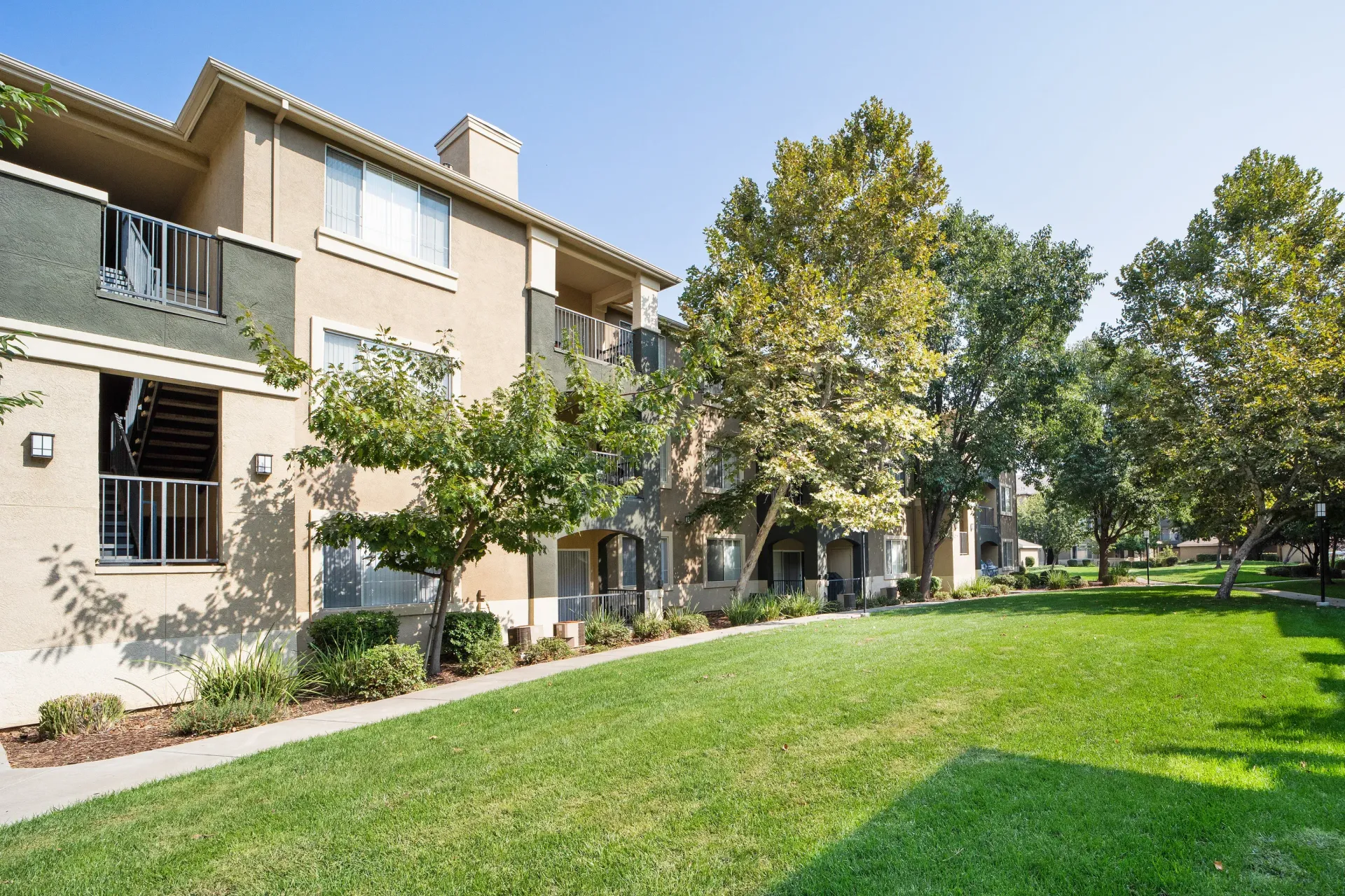 Exterior view of a modern apartment community with a grassy lawn and trees at Cross Pointe apartments in Antioch, CA.