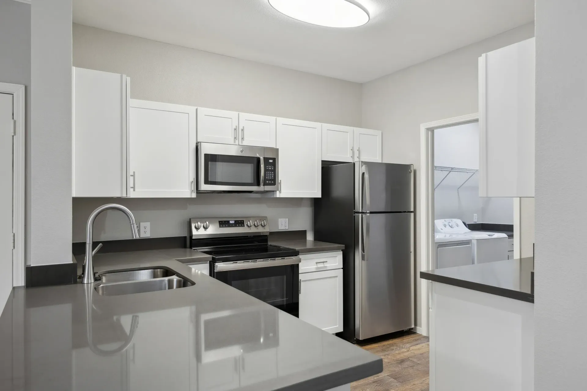 Modern apartment kitchen with white cabinets, gray countertops, and stainless steel appliances at Cross Pointe apartments in Antioch, CA.