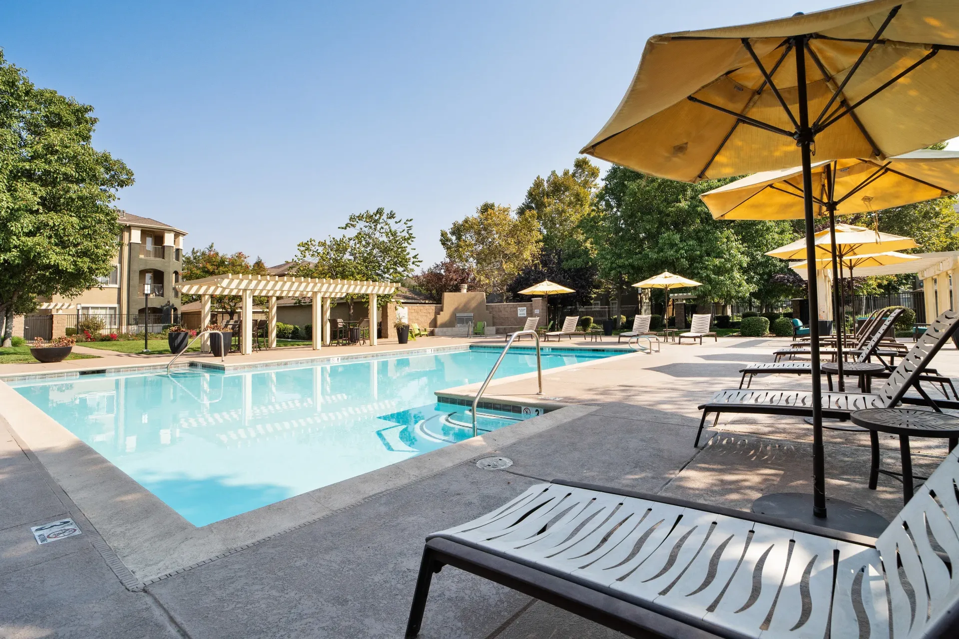 Outdoor pool area with lounge chairs and umbrellas at a residential complex at Cross Pointe apartments in Antioch, CA.