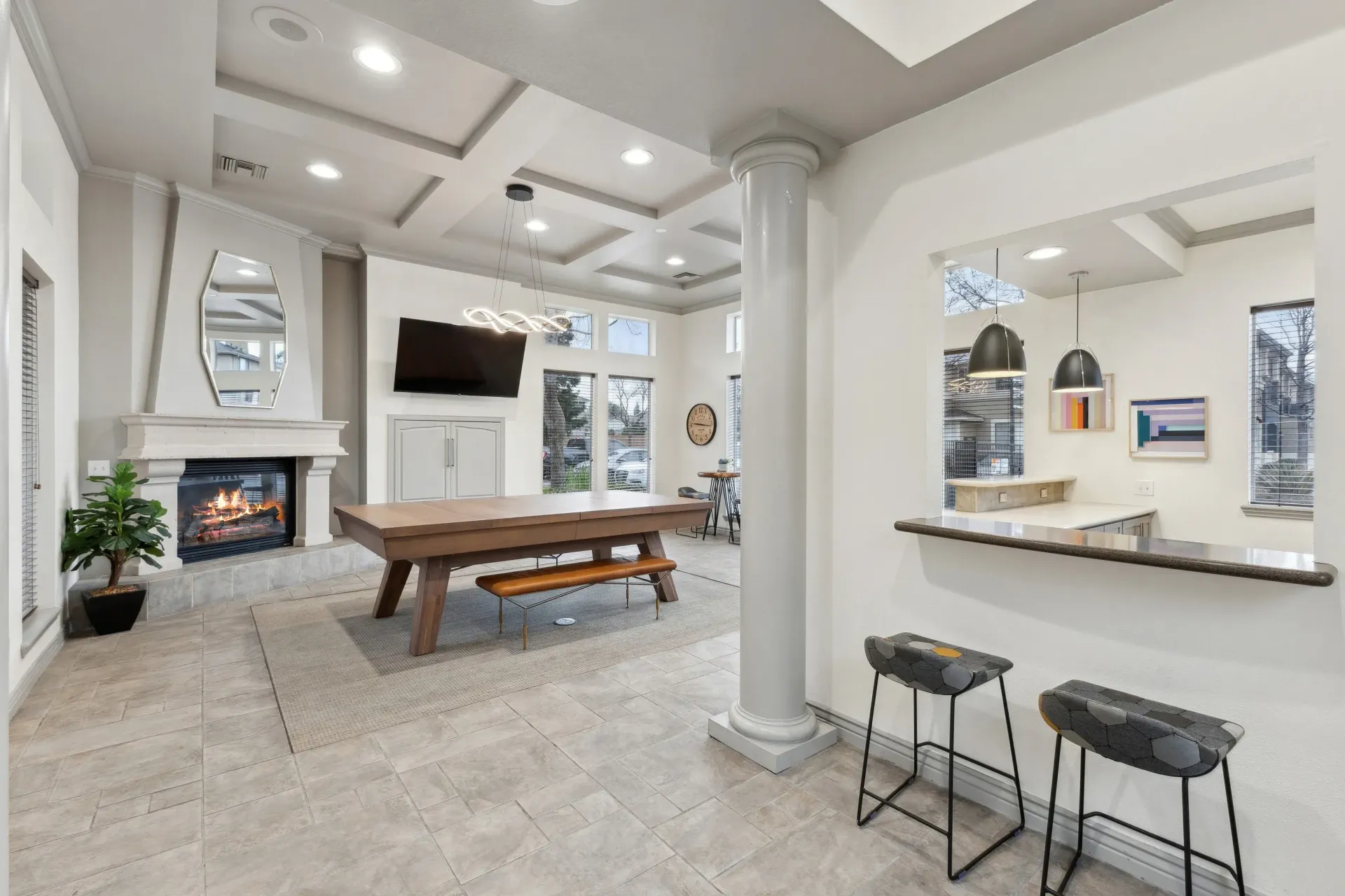 Bright community lounge with a fireplace, large wooden table, mounted TV, and bar seating at Cross Pointe apartments in Antioch, CA.