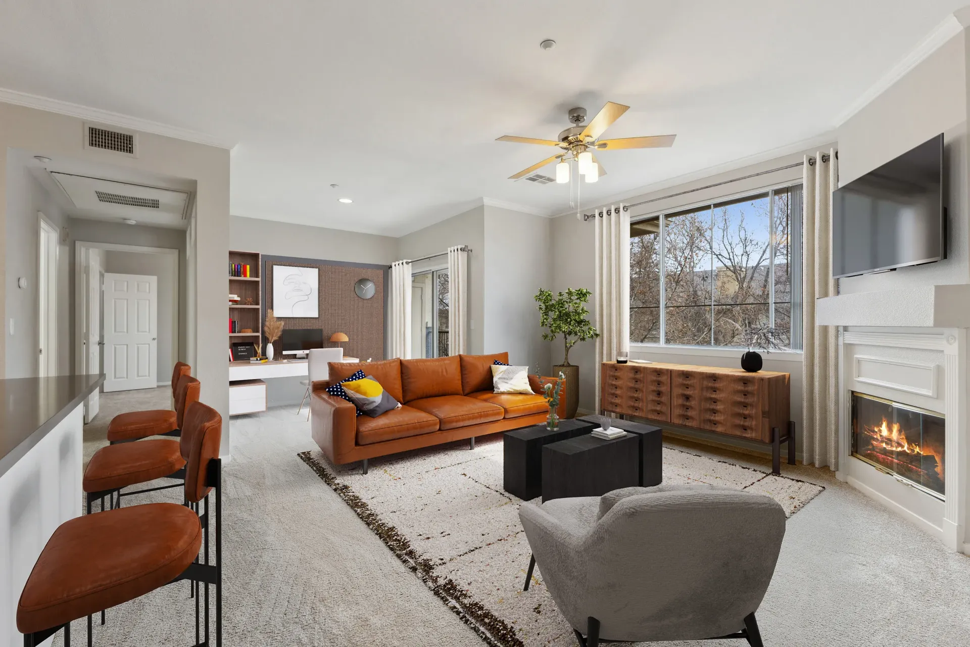 Bright apartment living room with tan leather sofa, fireplace, wall-mounted TV, and large window at Cross Pointe apartments in Antioch, CA.