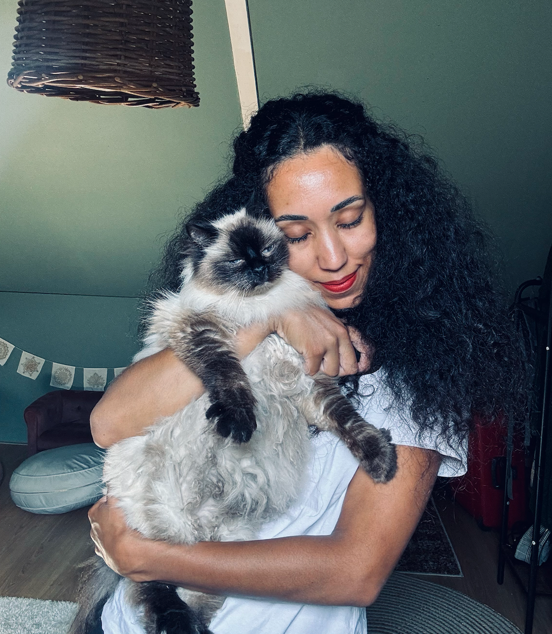 Vrouw met een pluizige zwart-witte kat binnenshuis, met een groene muur en slingers op de achtergrond.