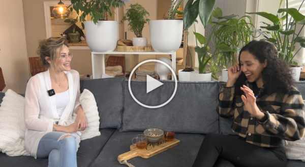 Twee vrouwen zitten op een grijze bank in een gezellige woonkamer en kletsen met een dienblad vol thee op tafel.