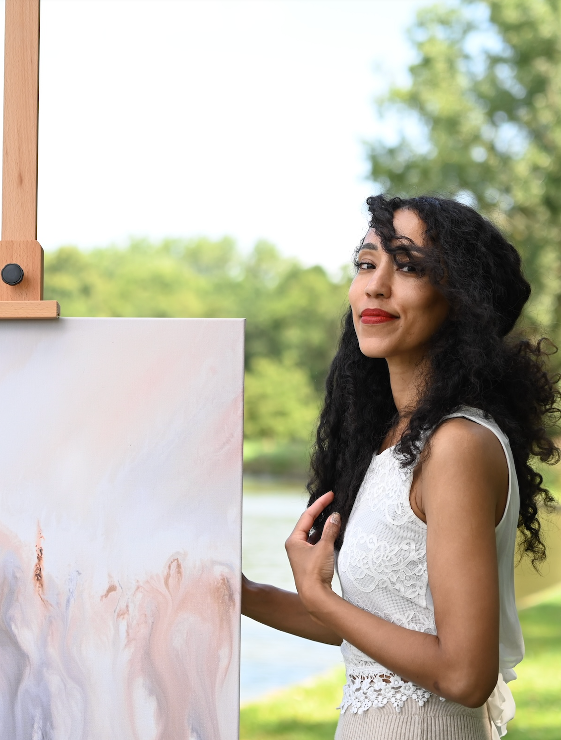 Een vrouw staat buiten op het gras naast een schilderij op een schildersezel