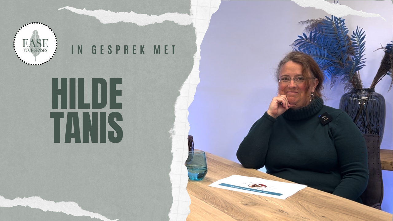 Hilde Tanis zit aan een tafel in een licht kantoor en glimlacht naast een bordje met haar naam.