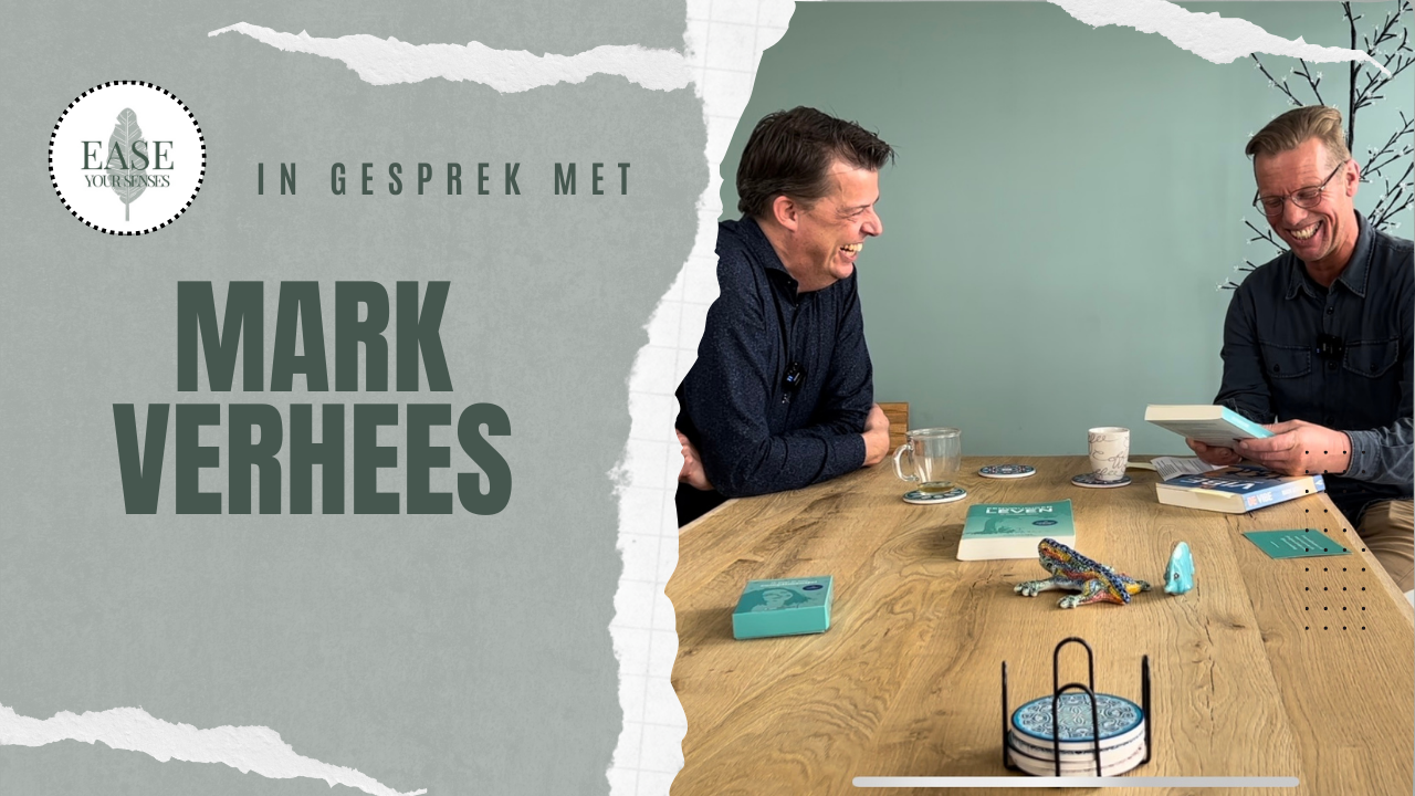 Twee mannen praten aan een houten tafel in een studio, met de tekst 