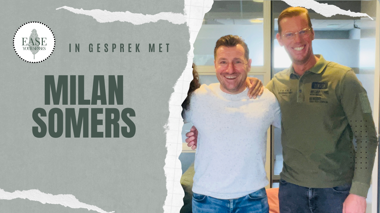 Twee lachende mannen poseren binnen naast een poster met de tekst 