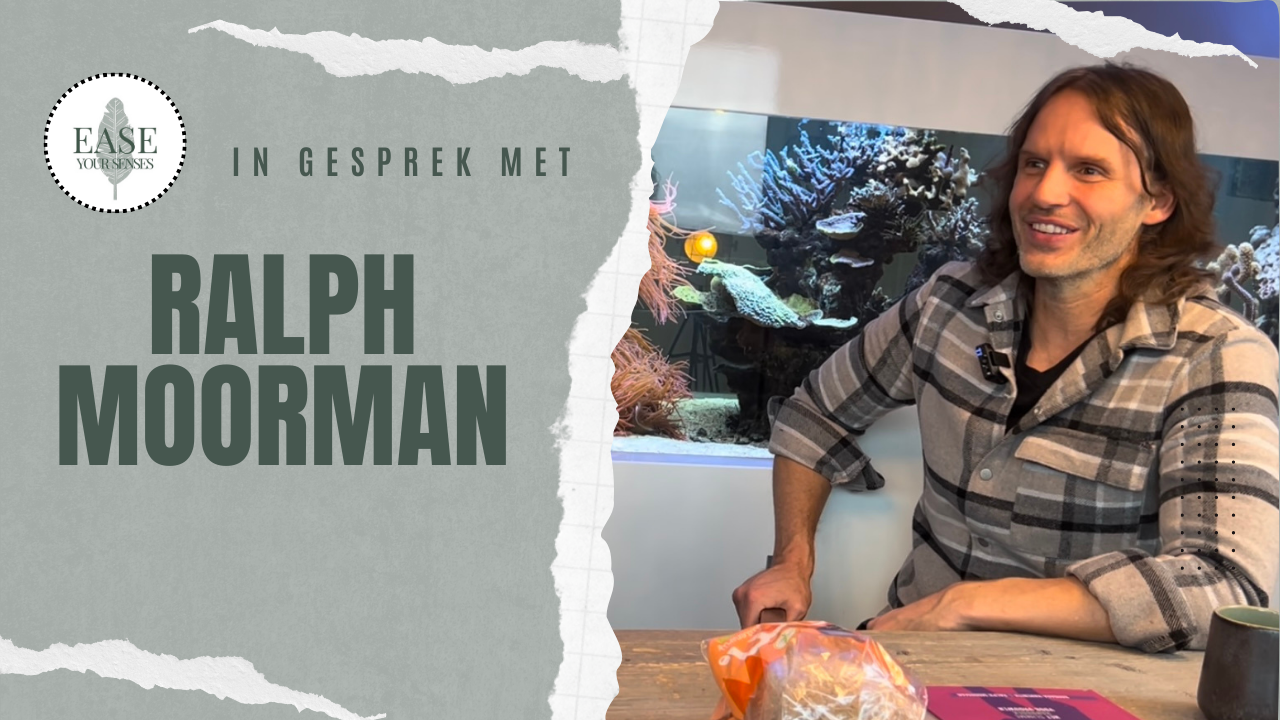 Ralph Moorman glimlacht aan een tafel in een lichte kamer, met de tekst 