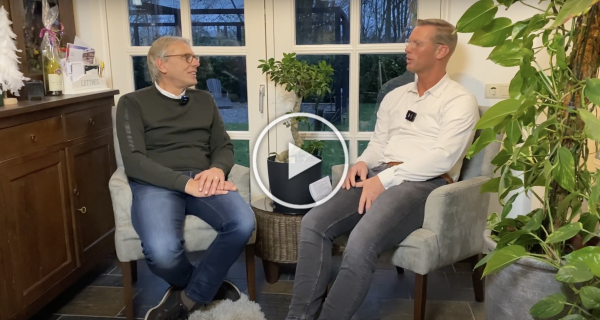Twee mannen zitten in een woonkamer en voeren een video-interview met elkaar.