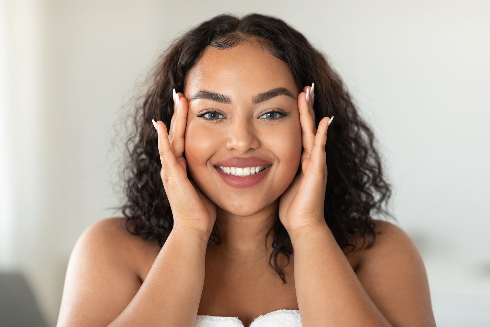 a woman is smiling and touching her face with her hands .