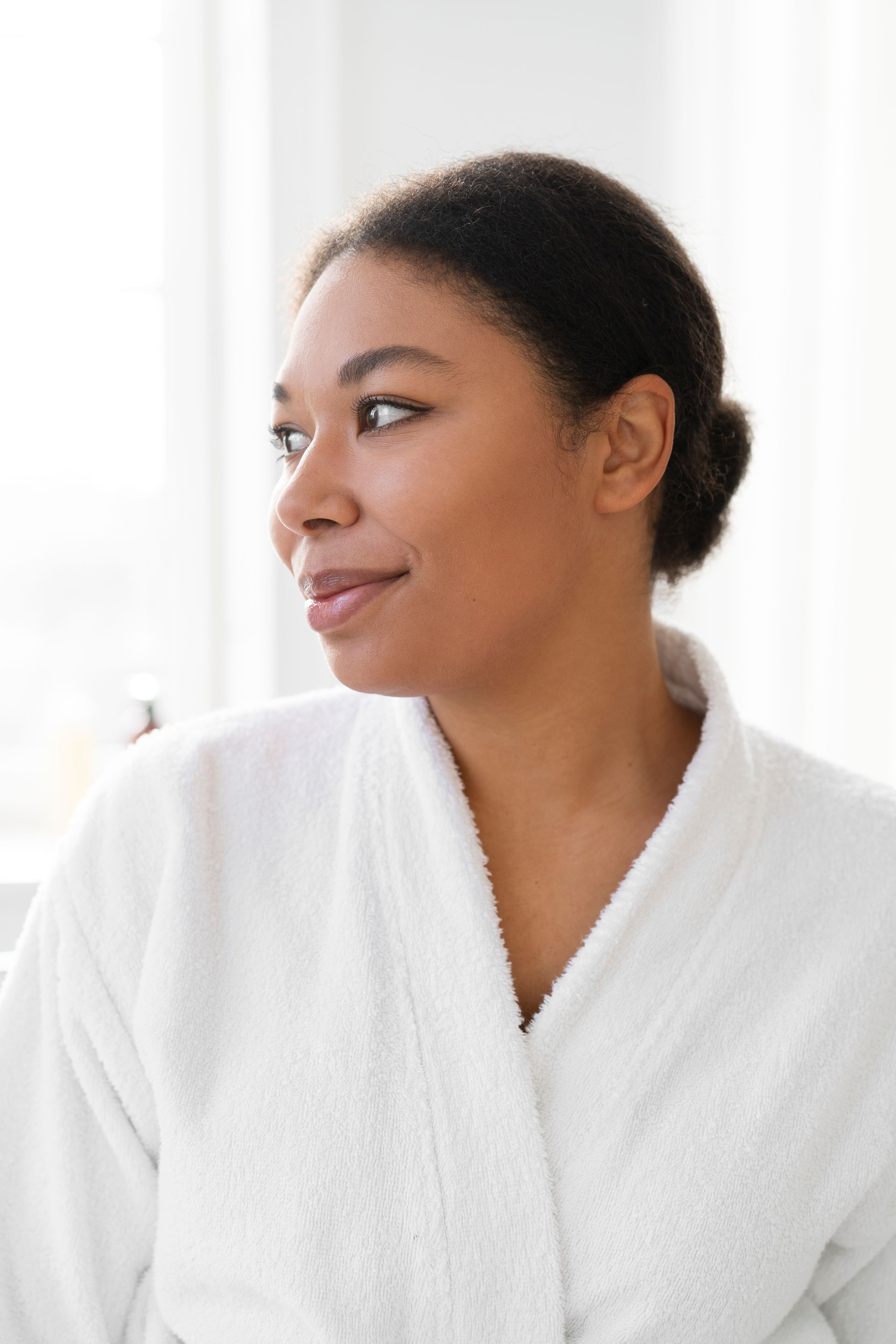 a woman in a white robe is looking out a window .