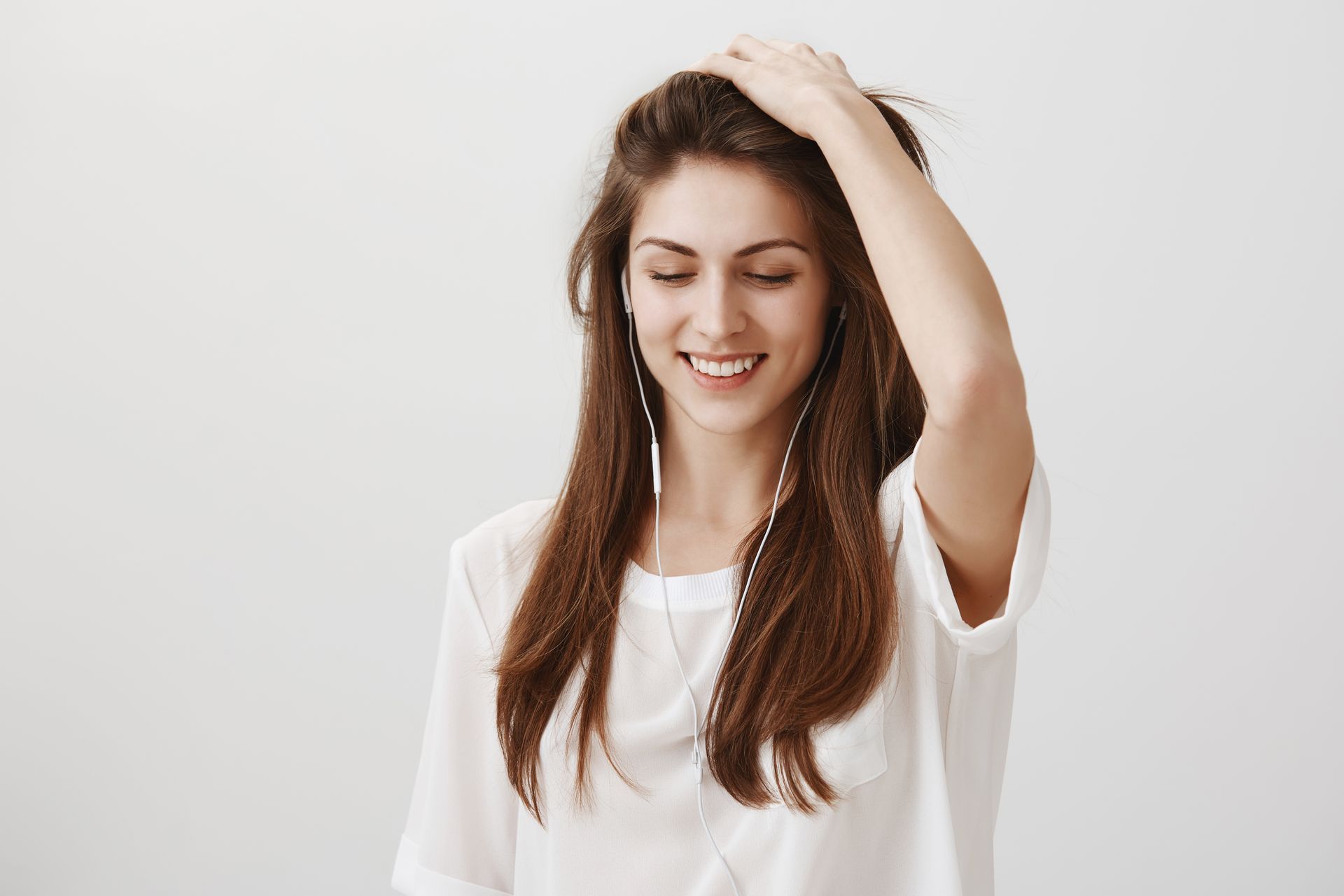 a woman wearing headphones is smiling and touching her hair .