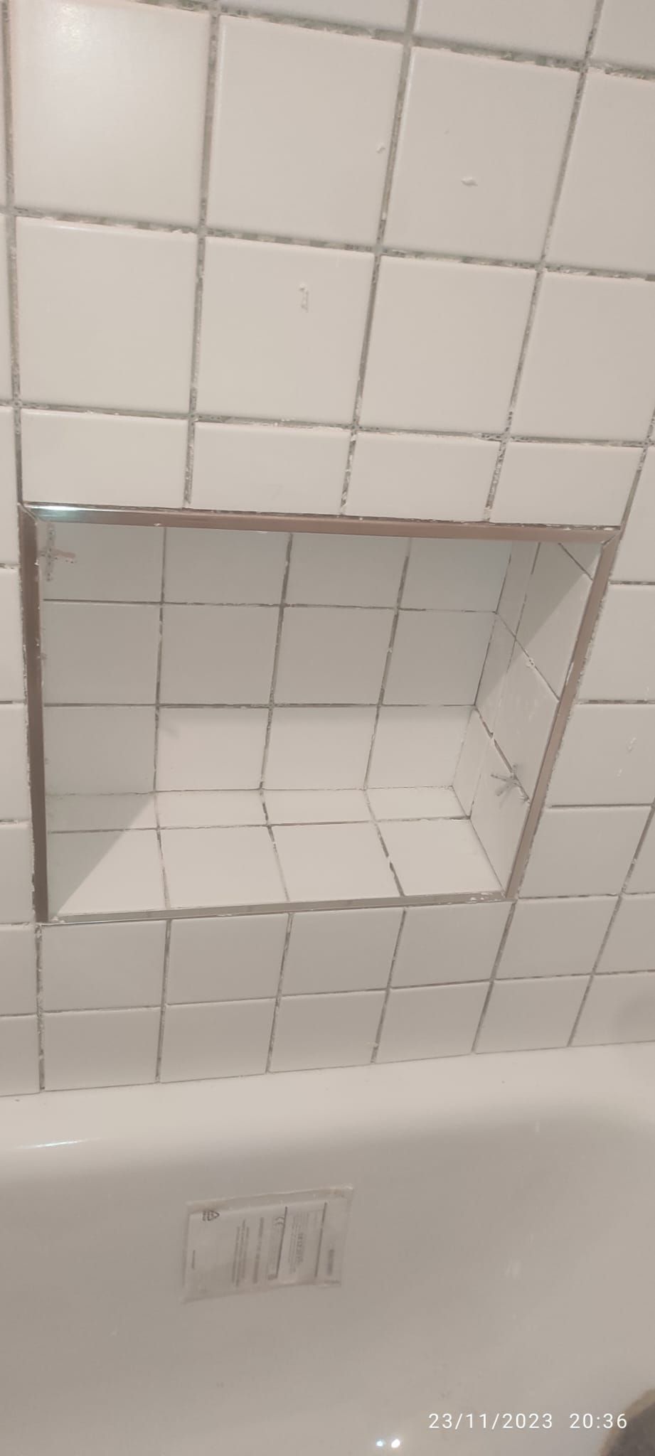 Parete della doccia piastrellata di bianco con mensola incassata sopra la vasca da bagno.