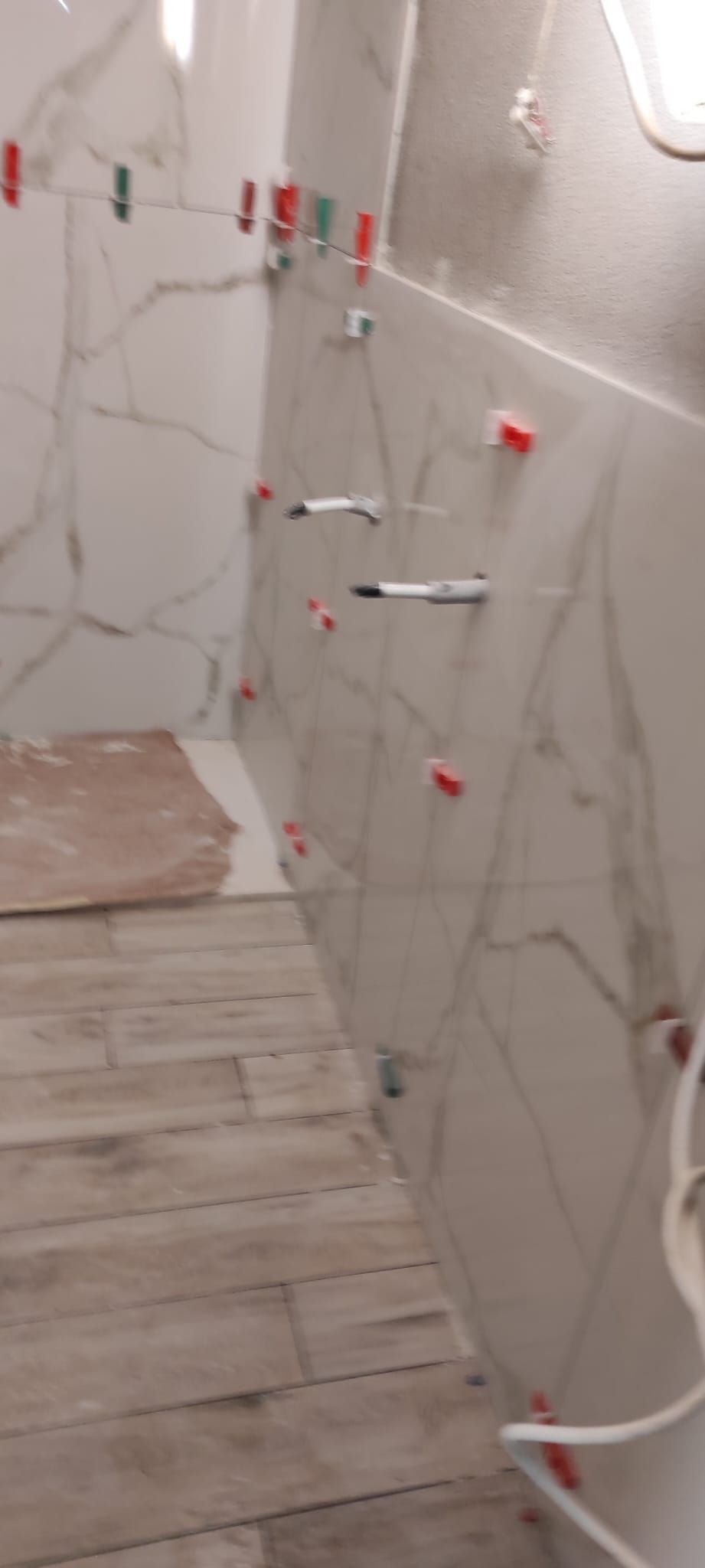 Parete della doccia del bagno in fase di ristrutturazione con piastrelle effetto marmo, tubature a vista e distanziatori di livellamento.