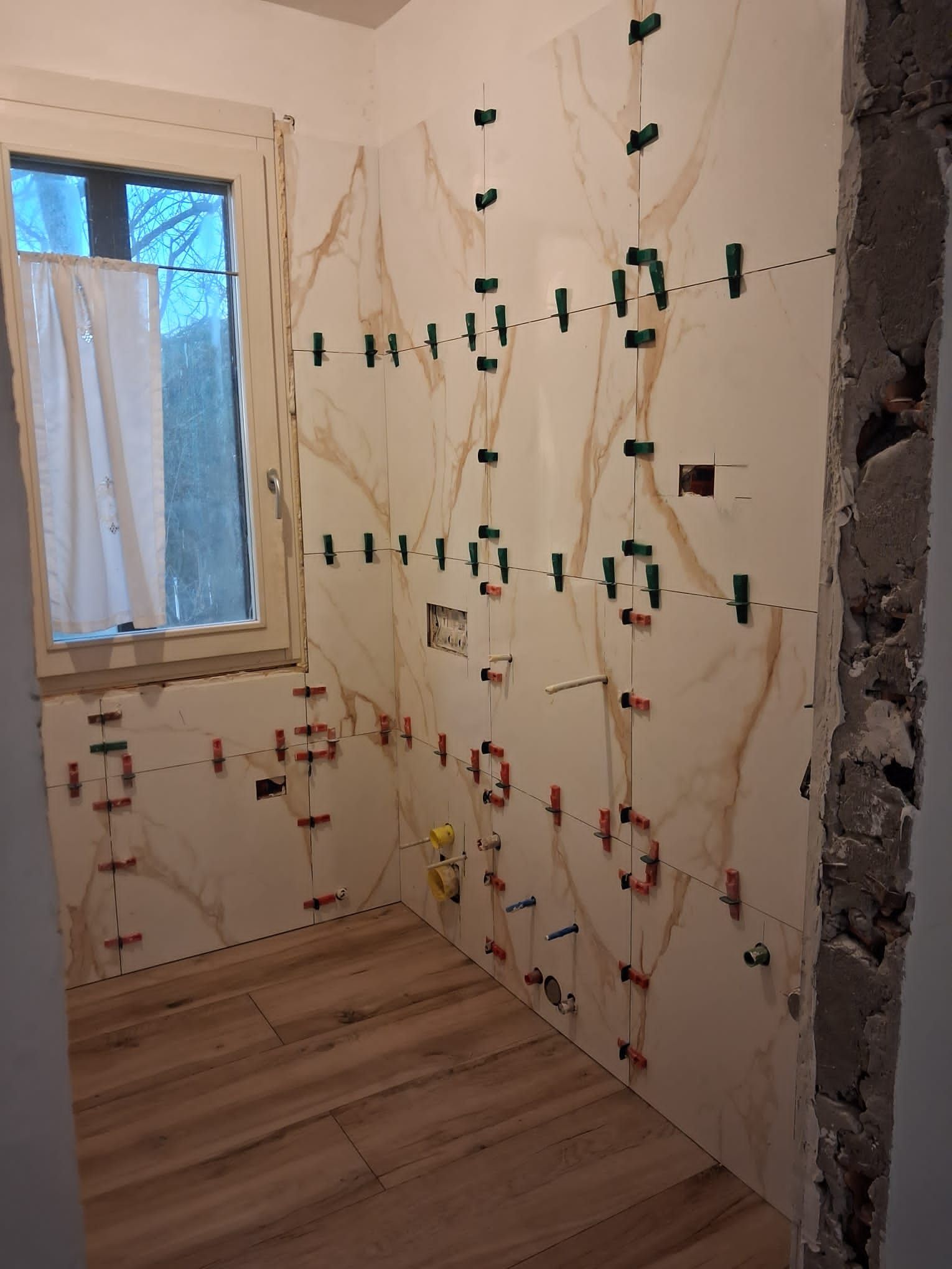 Parete del bagno ristrutturata con cavi elettrici, prese e una finestra sulla sinistra.