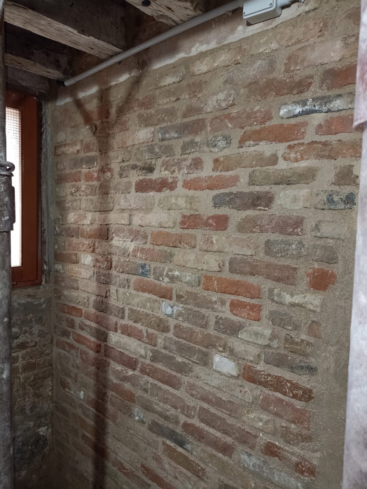 Parete in mattoni a vista all'interno di una stanza rustica con travi in legno e davanzale di una finestra.