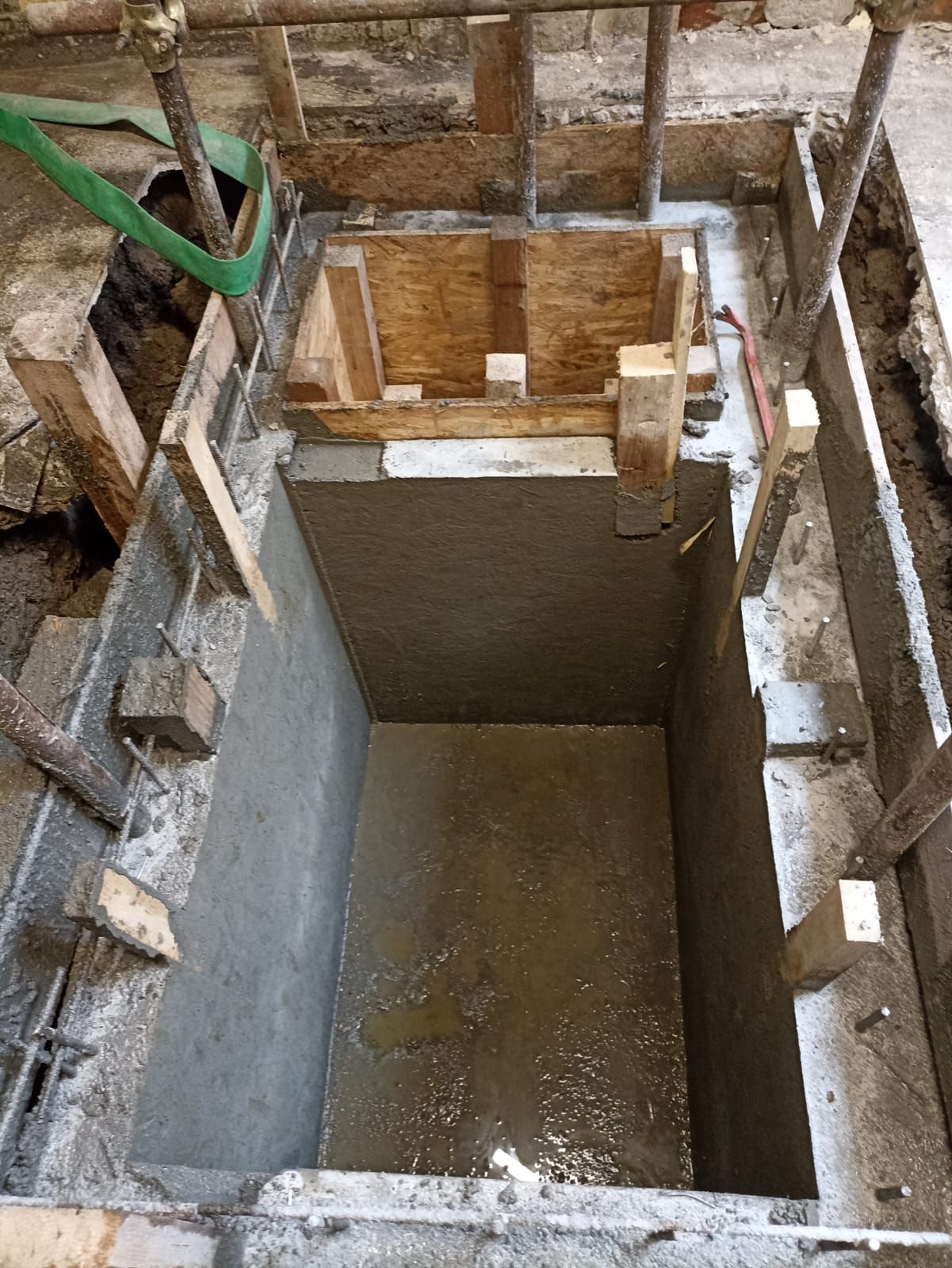 Fossa di costruzione a cielo aperto con pareti in cemento fresco e struttura in legno nella parte superiore.