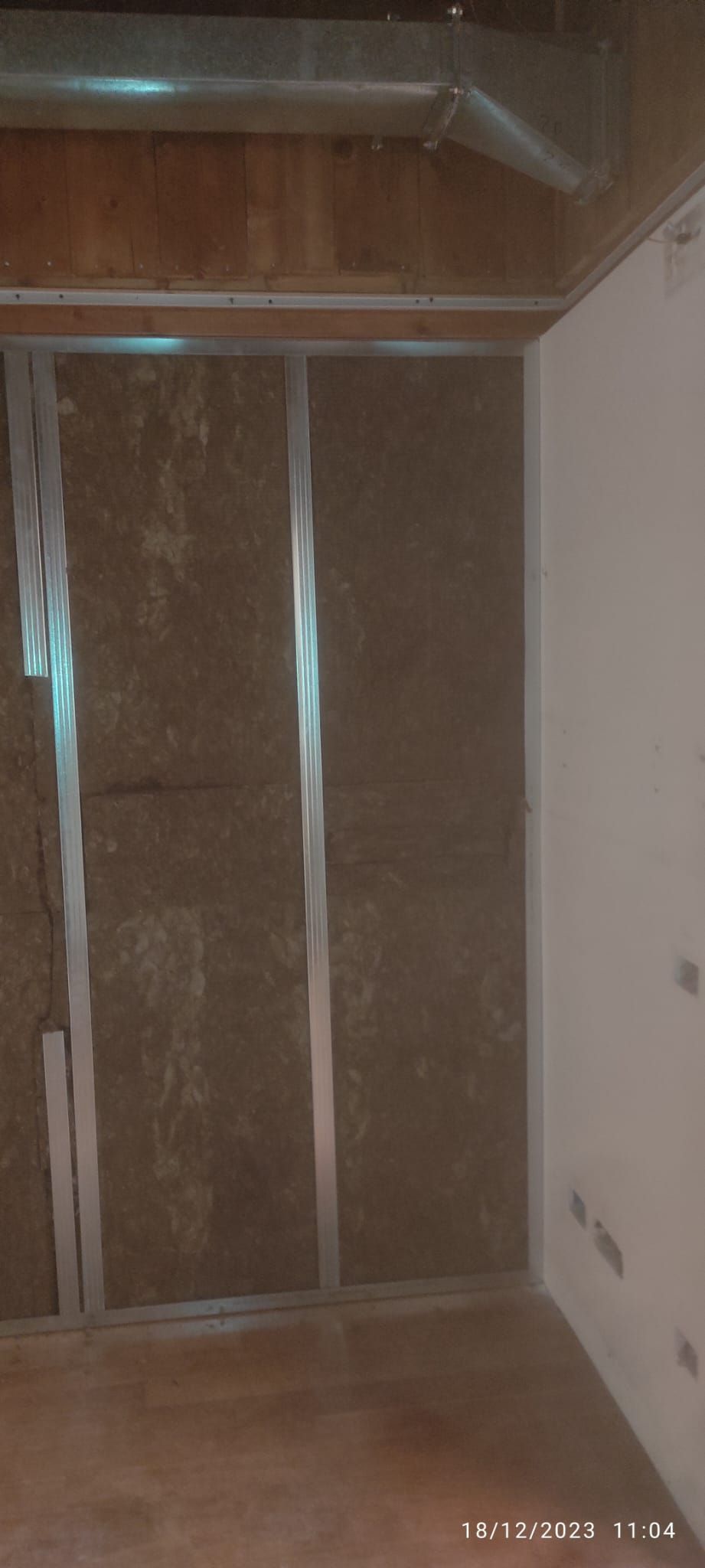 Armadio vuoto non rifinito con ripiani e appendiabiti in legno, pareti marroni e pavimento piastrellato.
