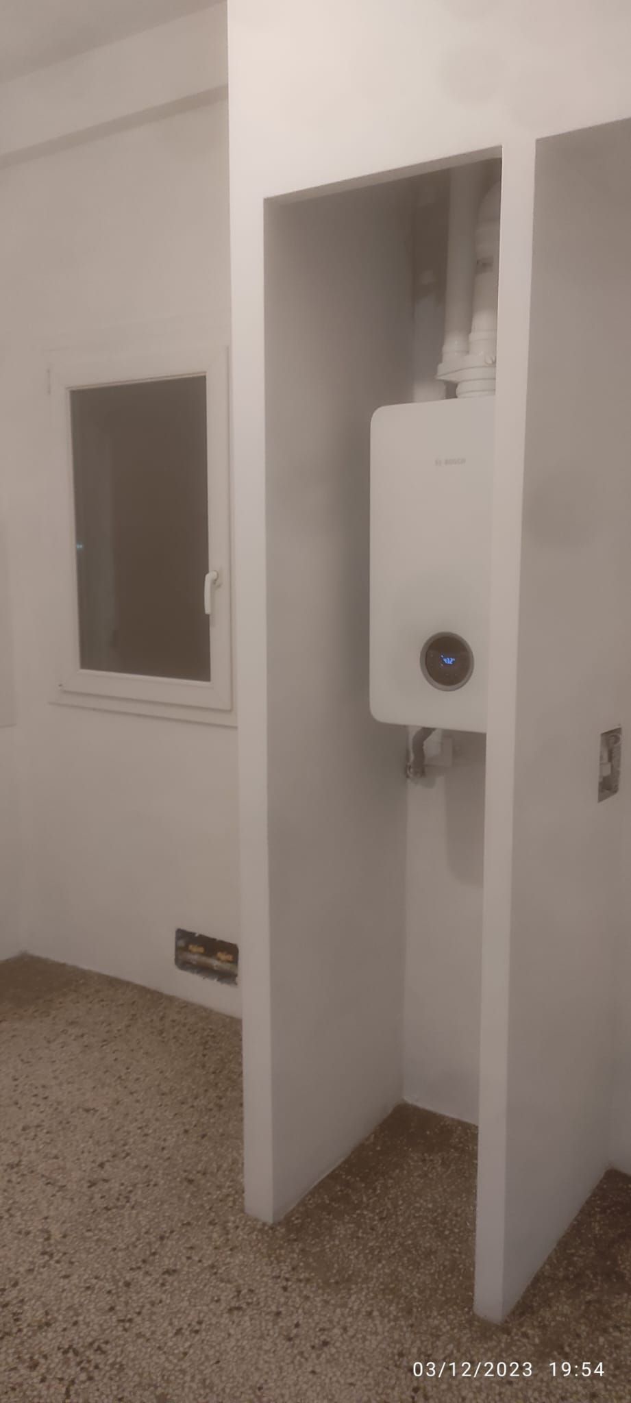 Cabina bagno bianca con una piccola finestra e un dispenser di carta igienica a parete.