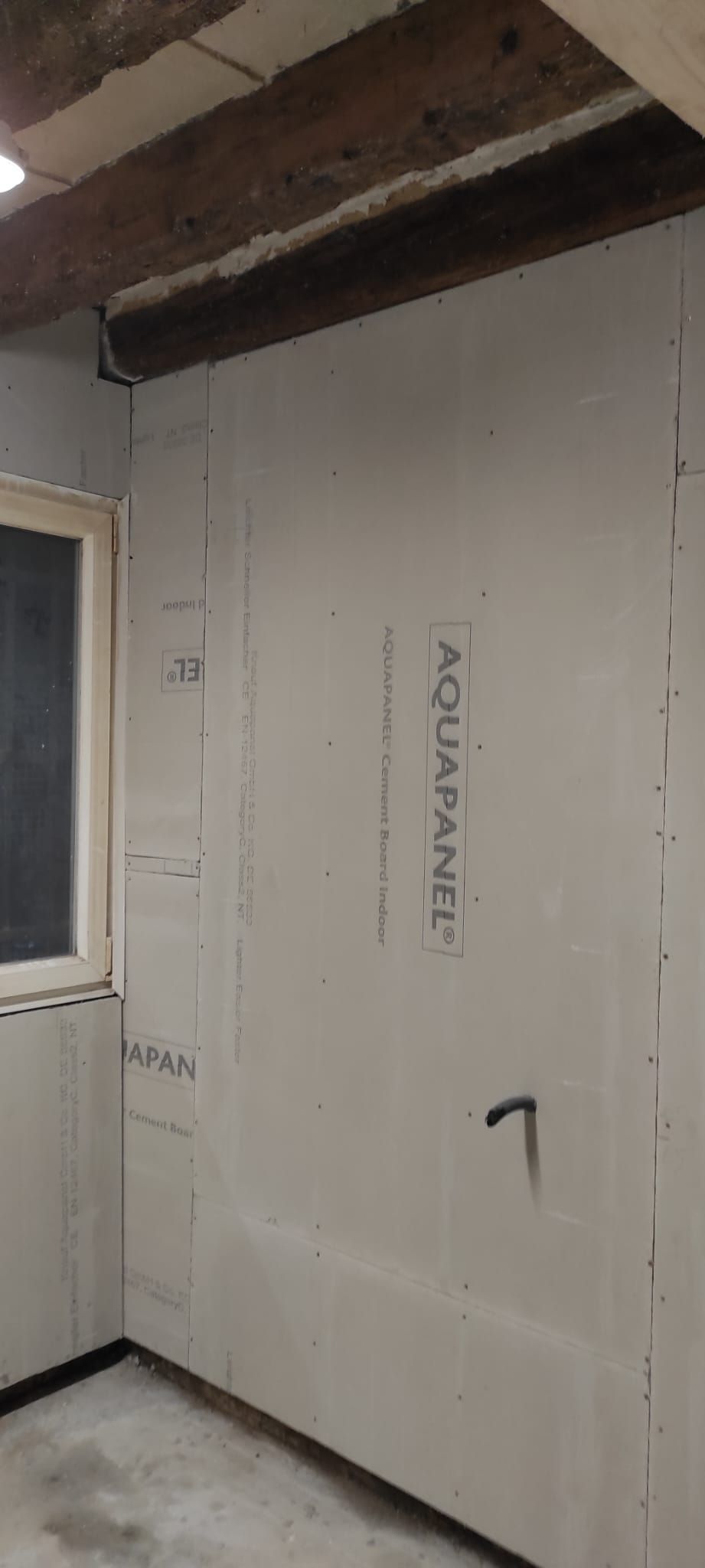 Piccola stanza non rifinita con pareti in cartongesso bianco, trave a vista sul soffitto e una finestra sulla sinistra.
