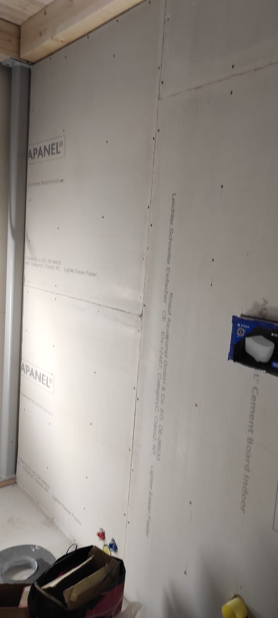 Parete in cartongesso parzialmente rifinita con giunture e scatola elettrica blu in una stanza in costruzione.