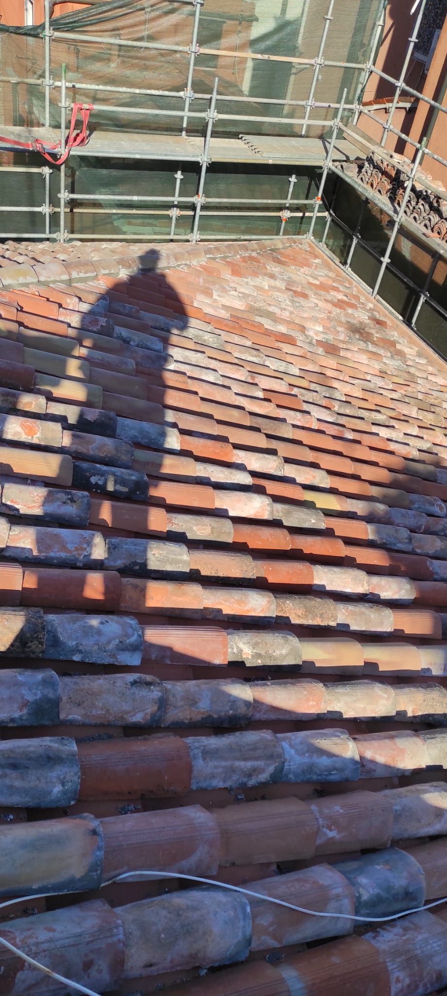 Ombra di una persona su un tetto di tegole, con impalcature e la parete di un edificio sullo sfondo.
